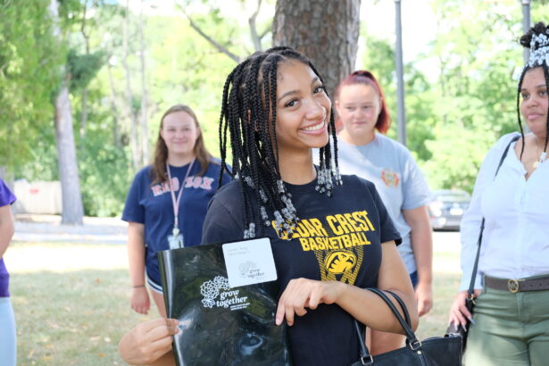 A young woman holding up a black orientation folder.