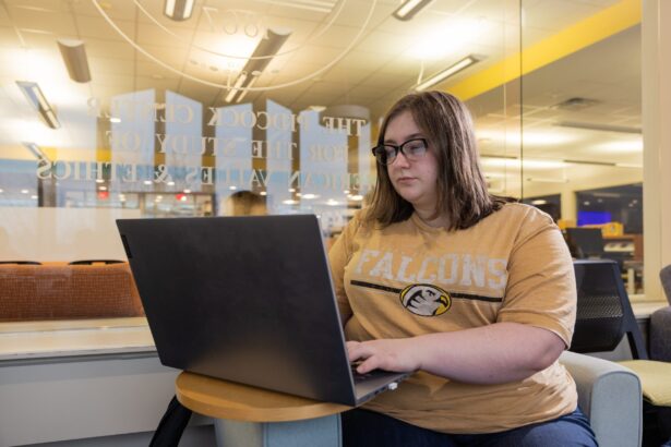 A young woman in a yellow shirt typing on a laptop in the library.