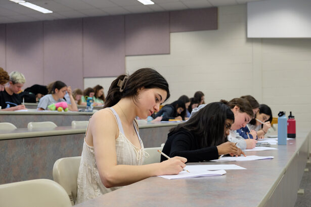 Students sitting at a desk in a lecture hall taking notes.