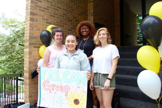 A group of students smile with a Falcon Group 14 sign