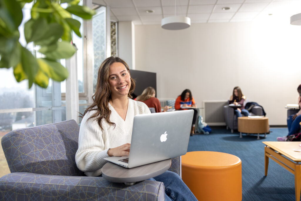 A young woman in a white sweater working on a mac laptop
