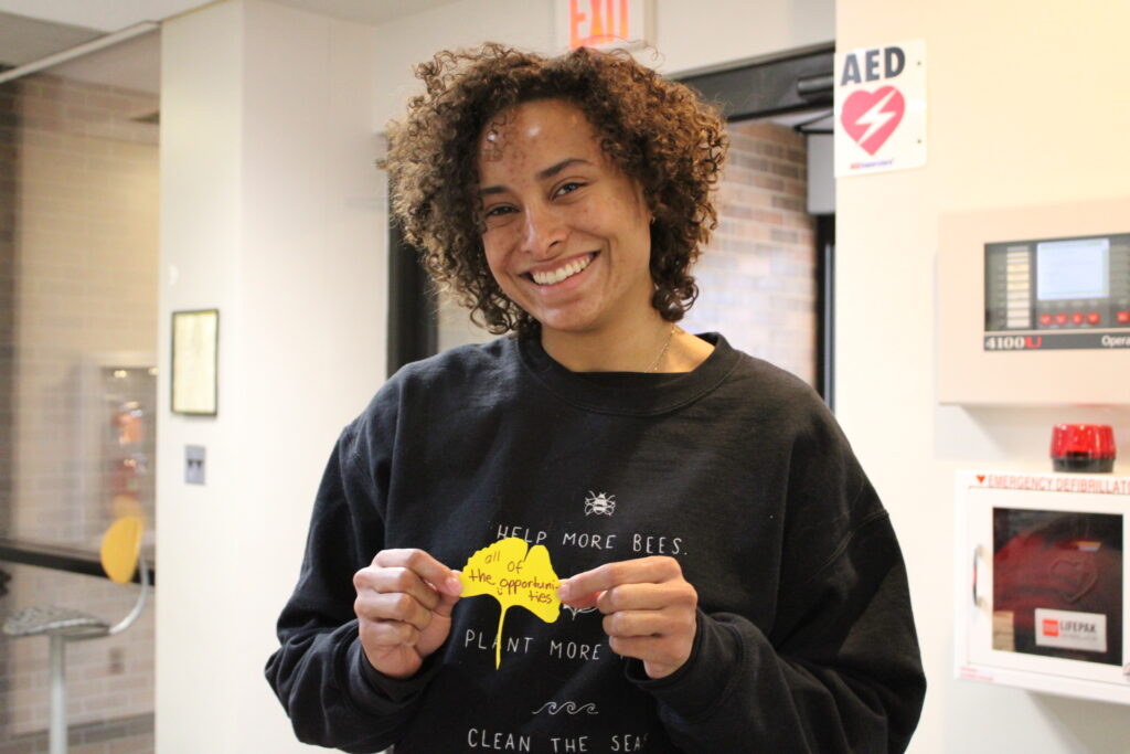 student stands holding a gingko leaf that says 