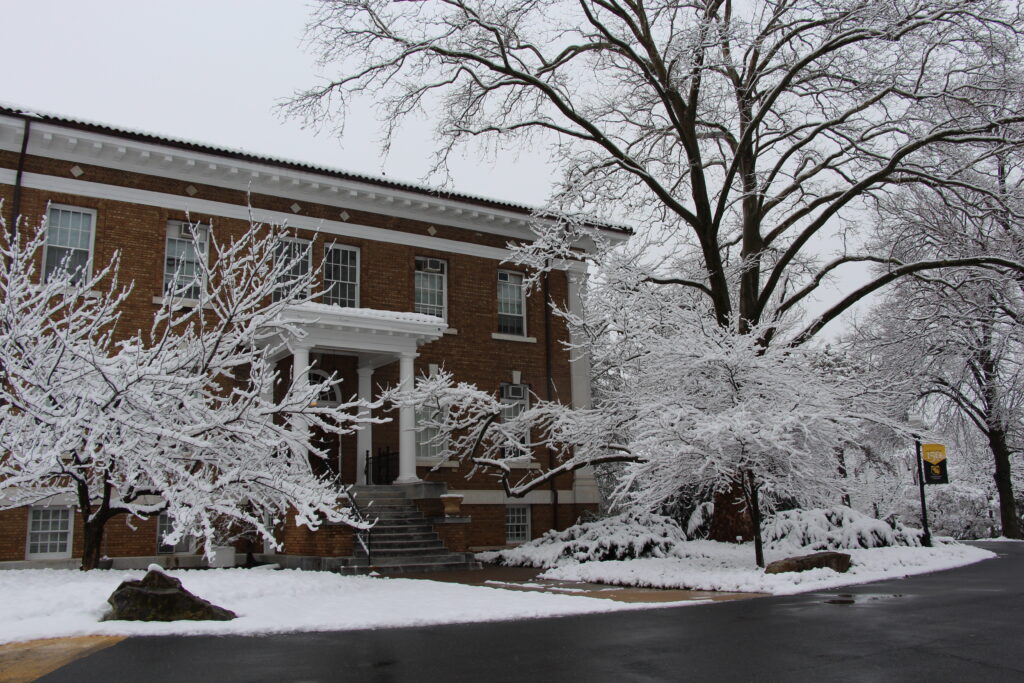 The back entrance of a building on campus covered in snow, two trees flanking the sidewalk with snow covering their limbs