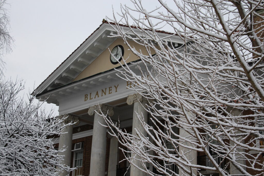 Picture depicts Blaney Hall during winter, snow on the limbs of tree branches nearby