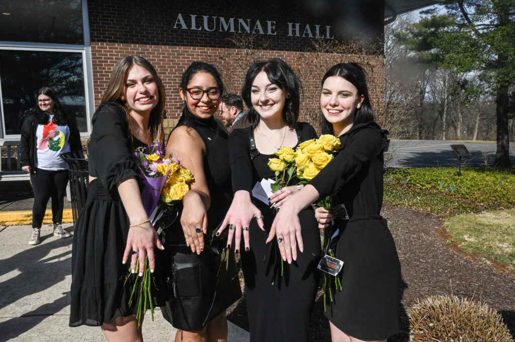 Four CCC students smiling, showing off their rings, and holding yellow flowers