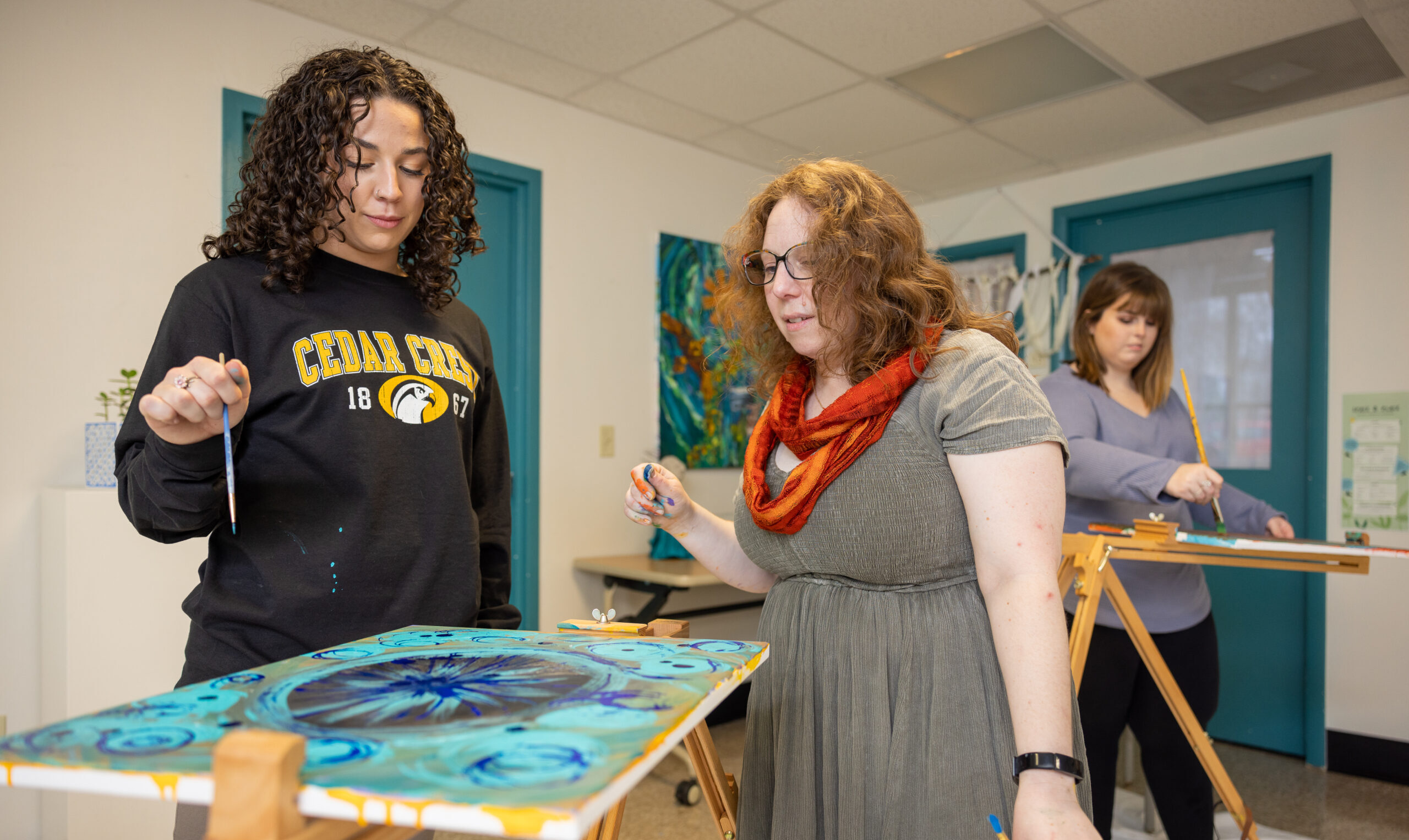 Art therapy student stands over her painting, in conversation with her professor