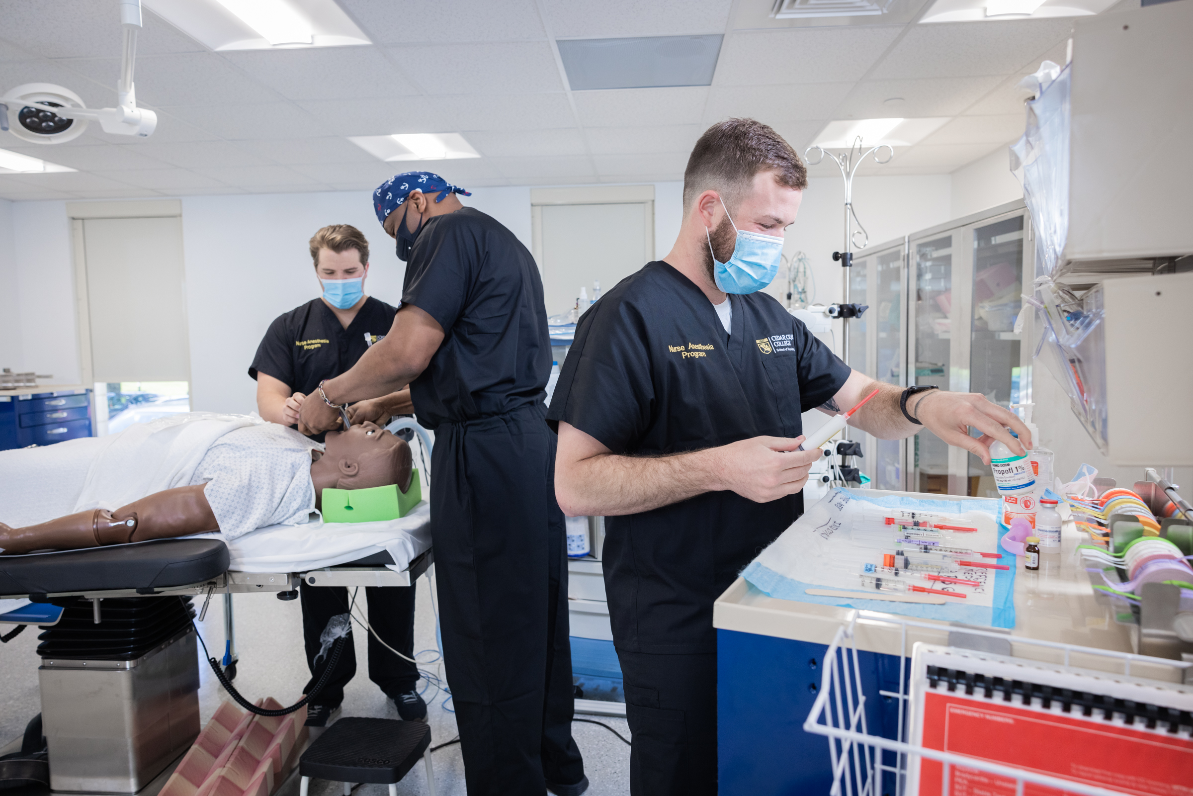 Three NAP students in blue scrubs and face masks working in a training lab