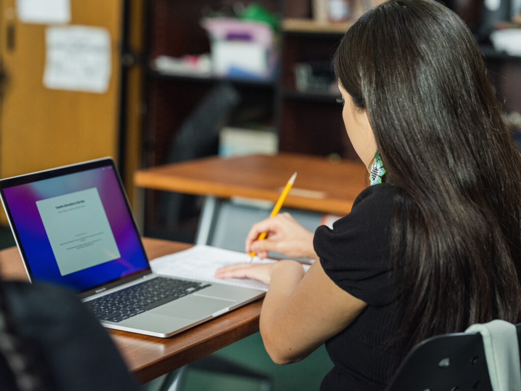 young person looking at a laptop and taking notes