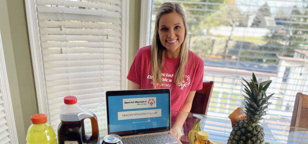 a woman in a red tshirt standing behind a laptop and a table with food on it